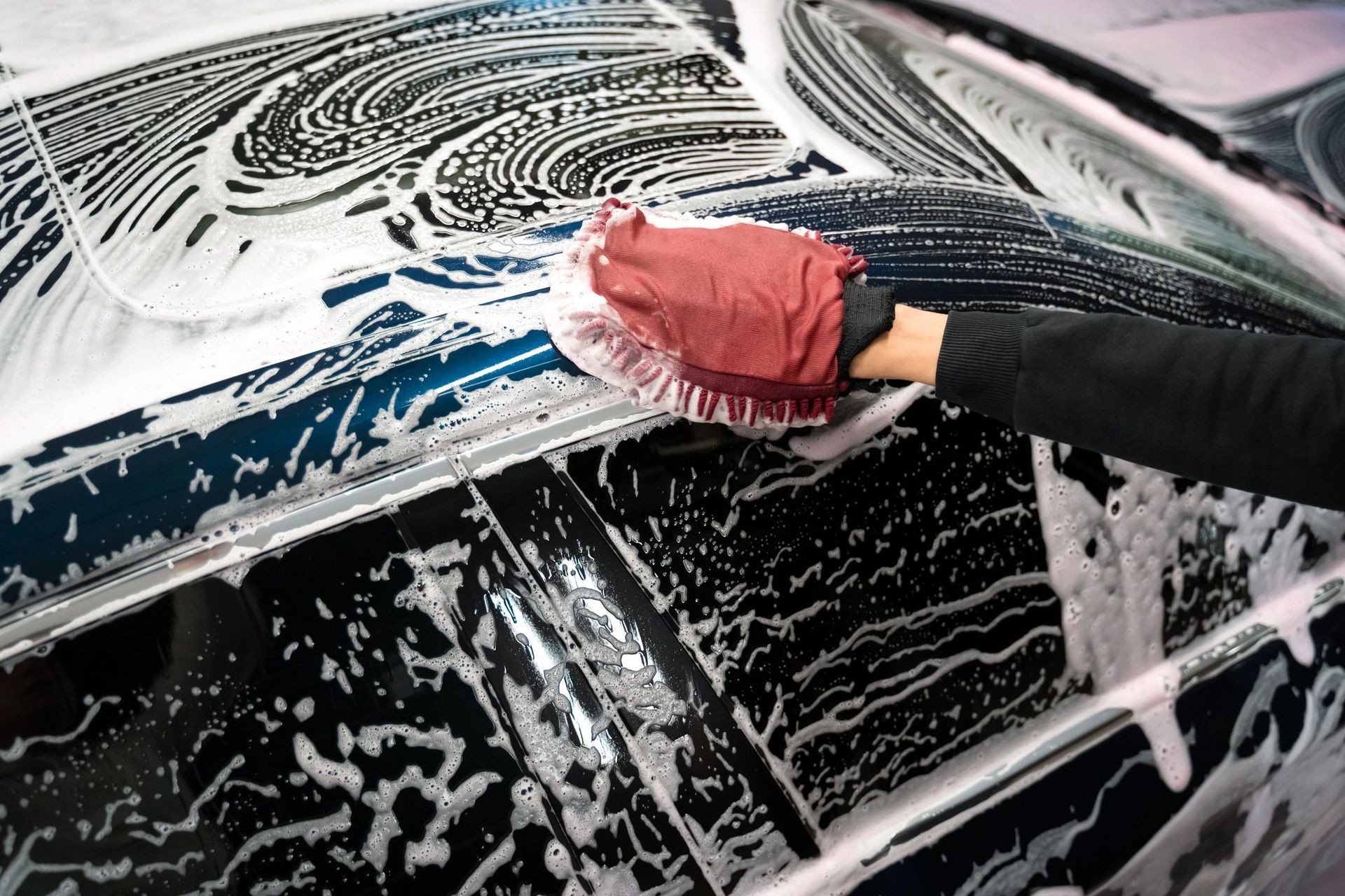 A person is washing a car with a brush and soap.
