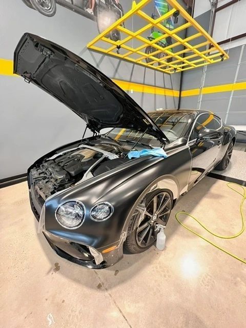 A black bentley with its hood open in a garage