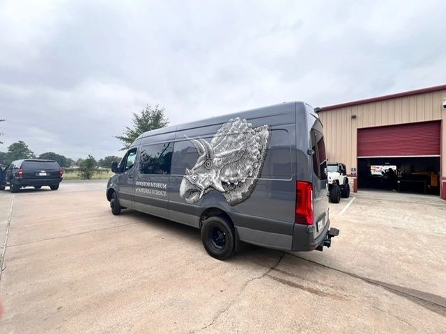 A van with a dinosaur on the side is parked in a parking lot.