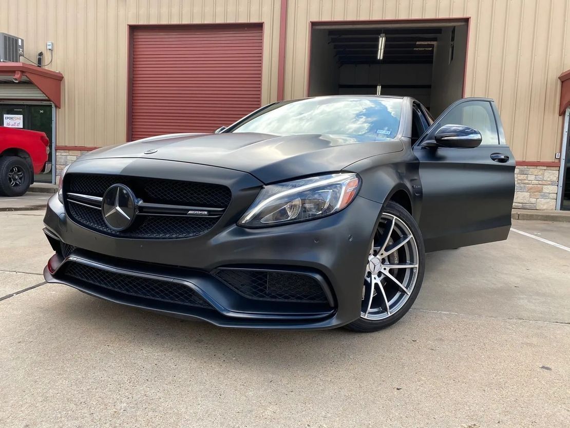 A black mercedes benz c63 amg is parked in front of a garage.
