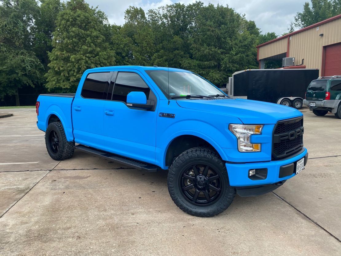 A blue ford f150 truck is parked in a parking lot.