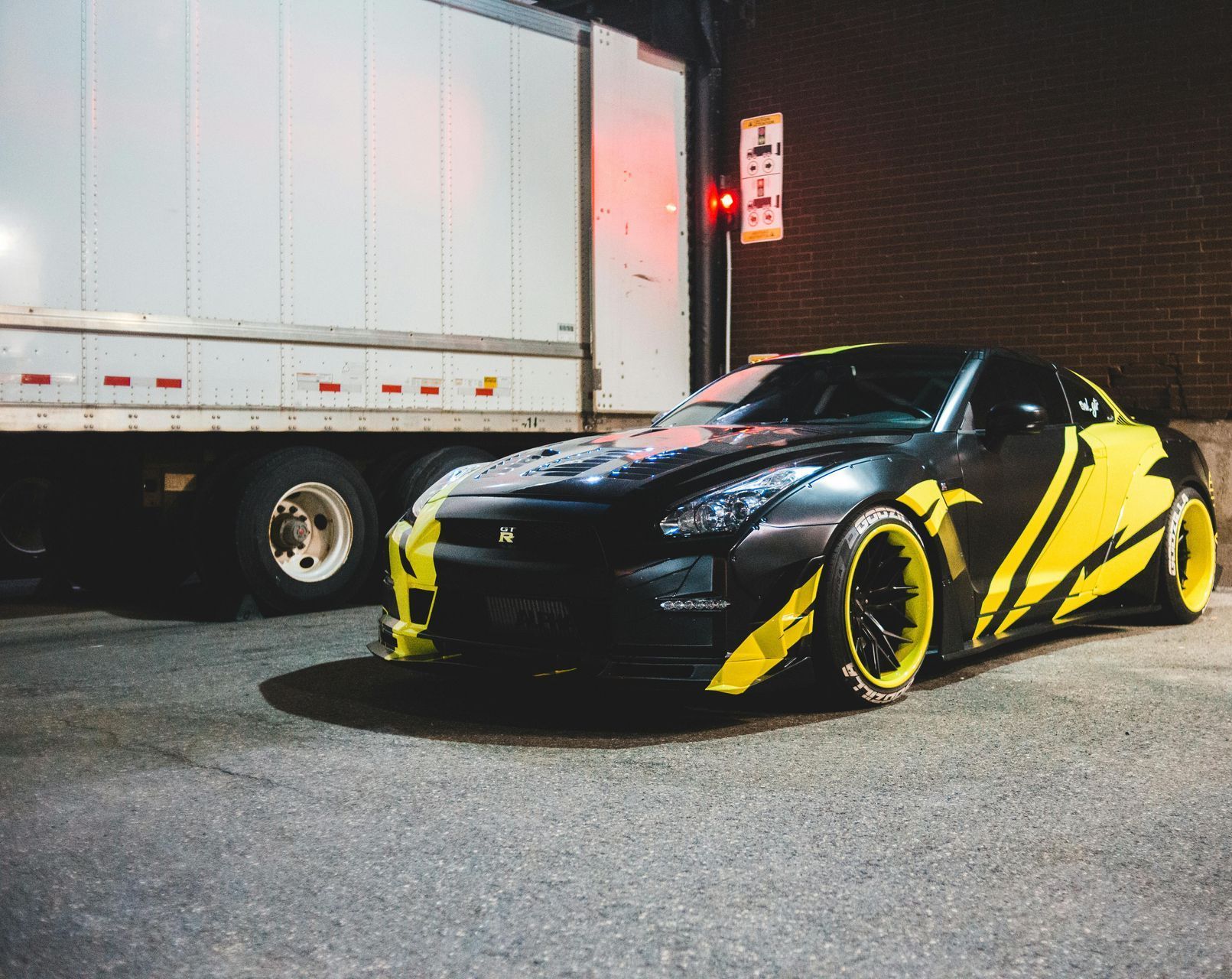 A black and yellow sports car is parked in front of a truck.
