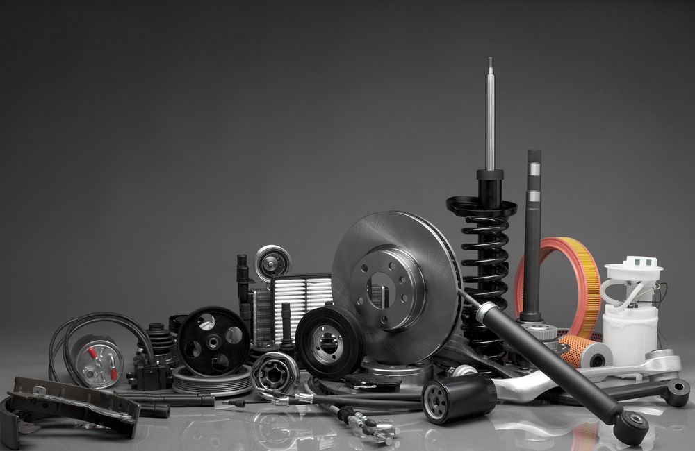 Pile of various car parts on a gray surface, including brake discs, suspension, and filters.
