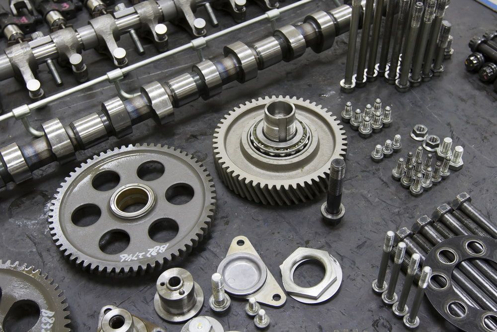 Engine parts, including gears, camshafts, and bolts, arranged on a dark surface. — Beenleigh Bearings in Beenleigh, Yatala