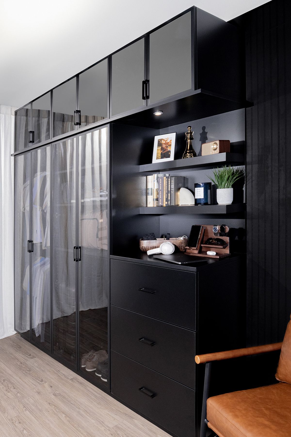 Black wardrobe wall with clear cabinets, open shelves, and a tan chair in a modern room