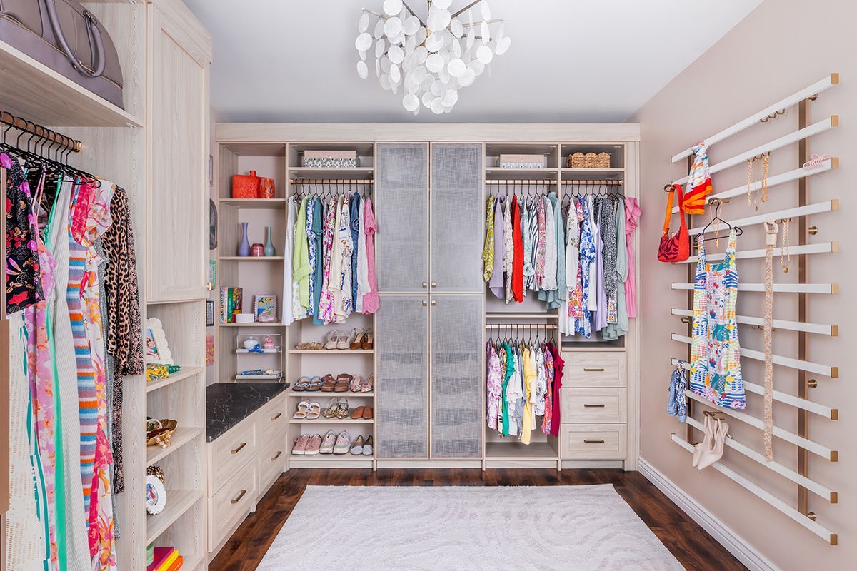 Bright walk-in closet with white shelves, hanging colorful clothes, drawers, and a chandelier