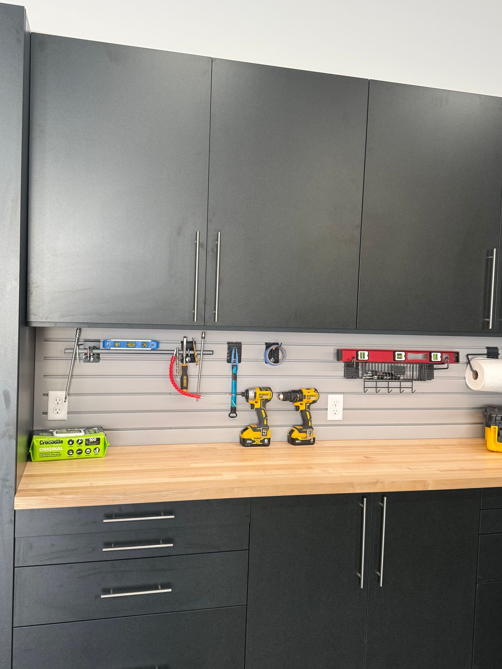 Modern garage workbench with black cabinets, wooden countertop, tools, and power outlets along the wall