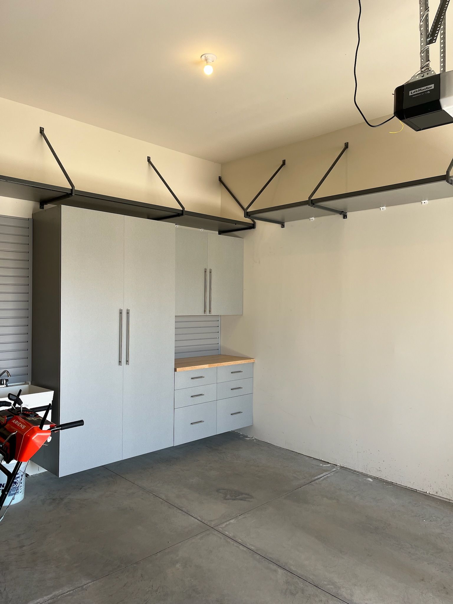 Garage interior with white cabinets, wall-mounted storage, and a motorcycle at left.