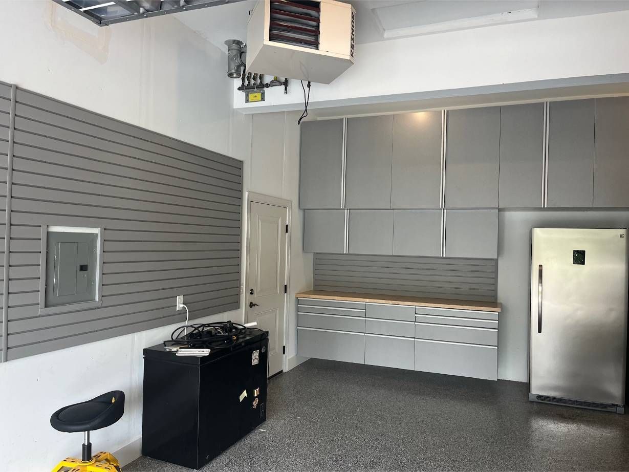 A garage with gray cabinets and a stainless steel refrigerator.