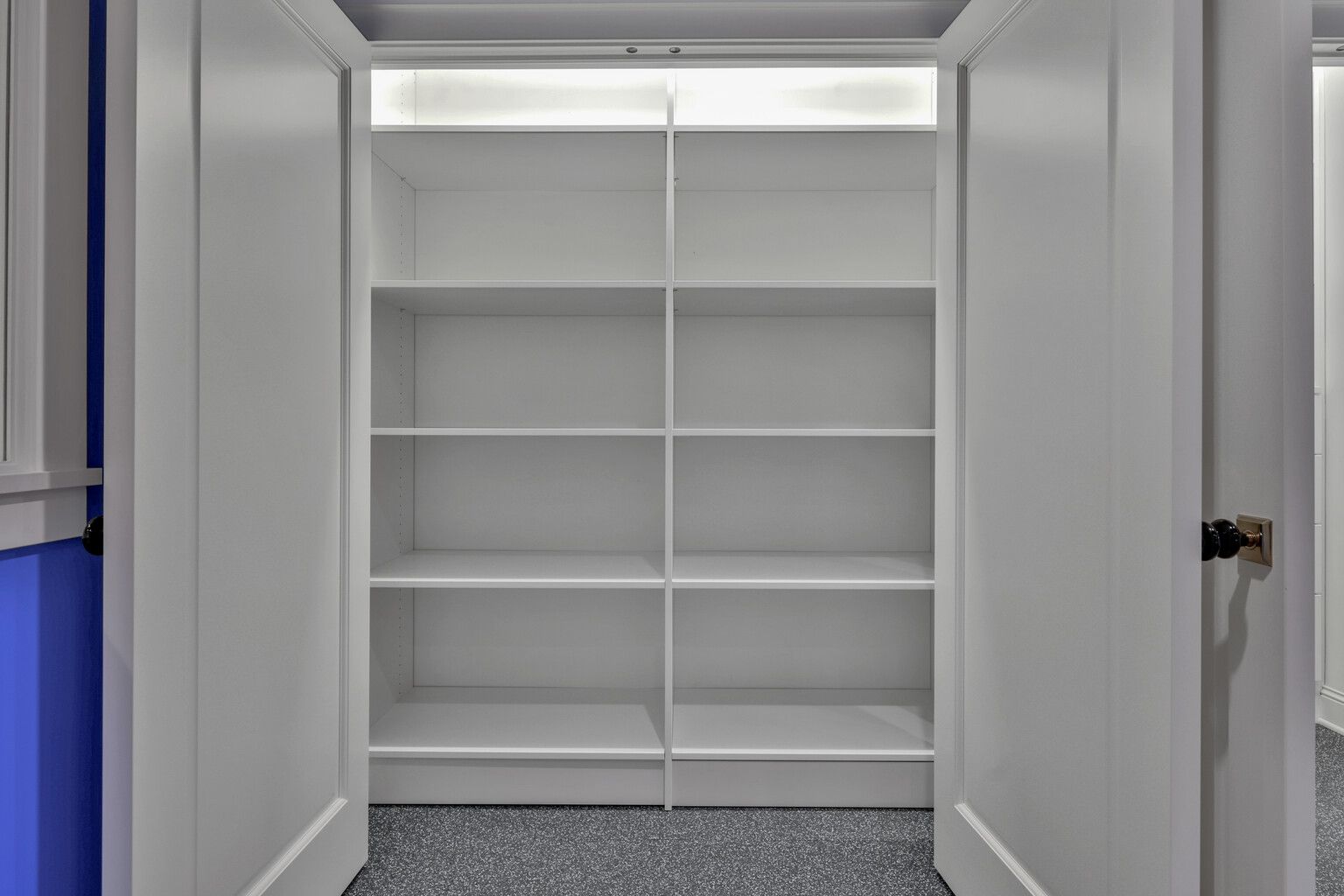 An empty walk in closet with white shelves and a blue wall.