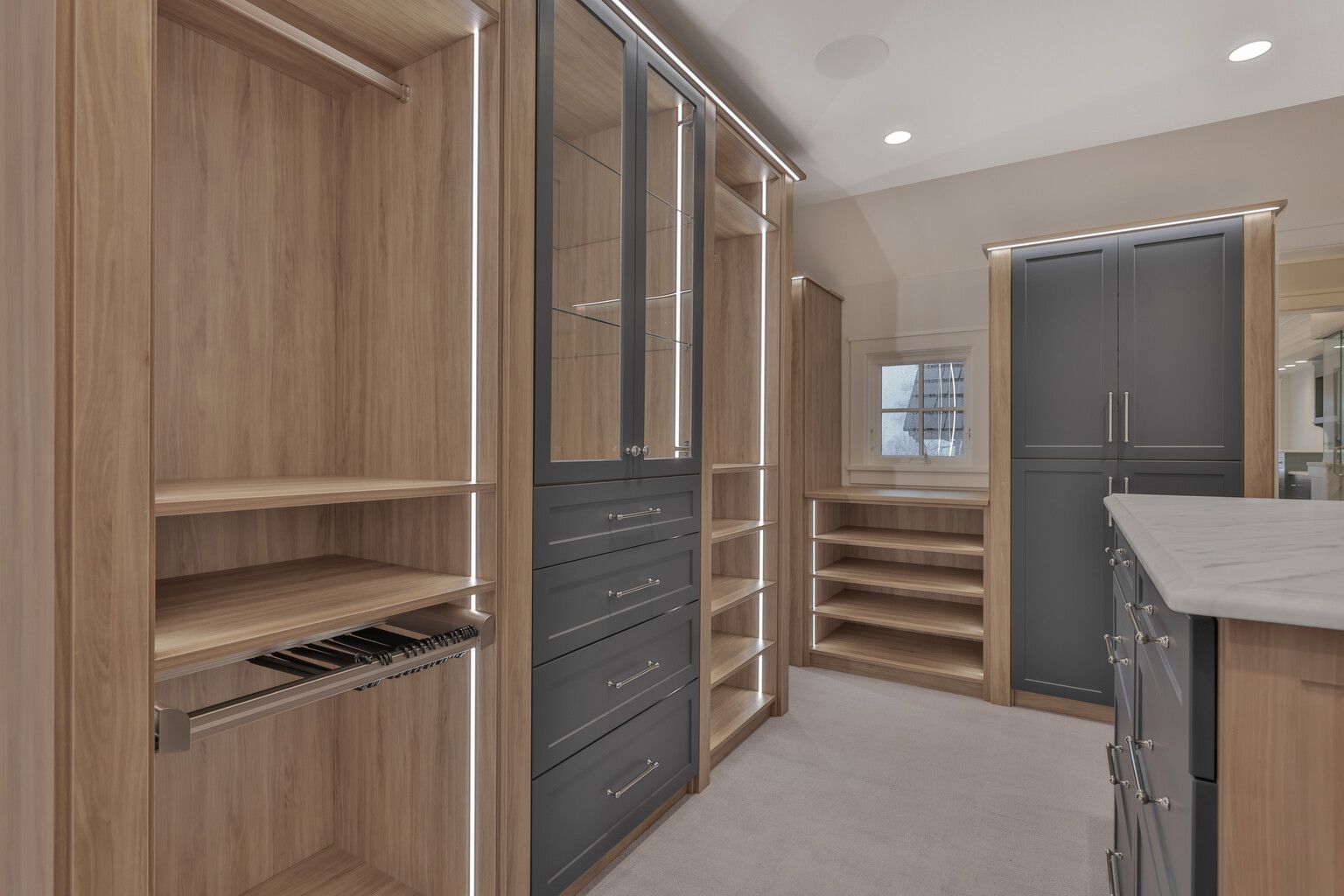 A walk in closet with lots of shelves and drawers and a kitchen in the background.