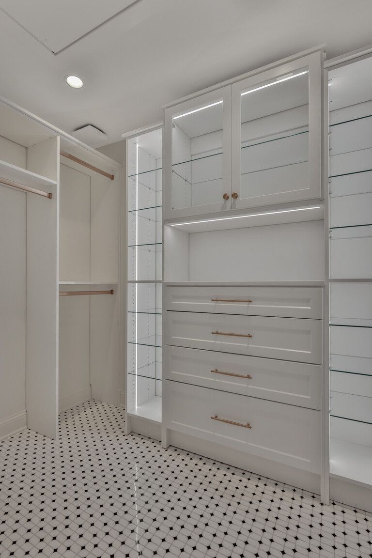 A walk in closet with white cabinets and drawers and a black and white tile floor.
