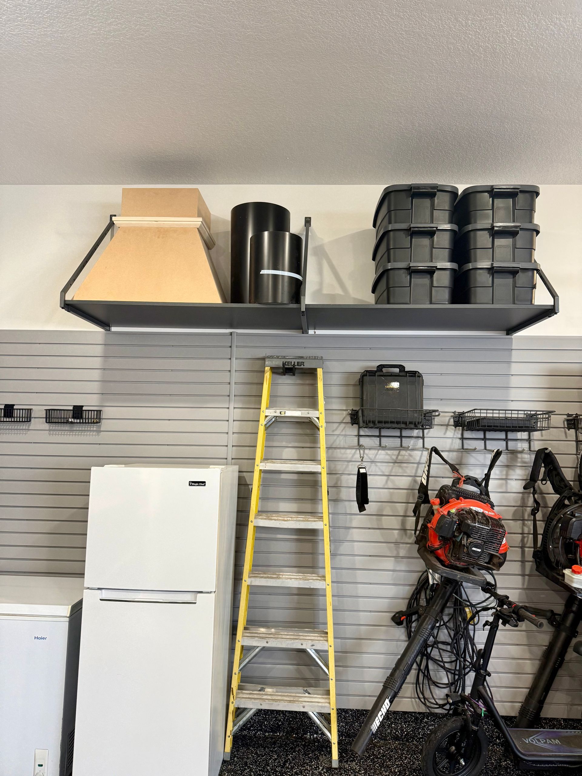 Garage wall shelves with storage bins, a ladder, and hanging bikes above a white refrigerator