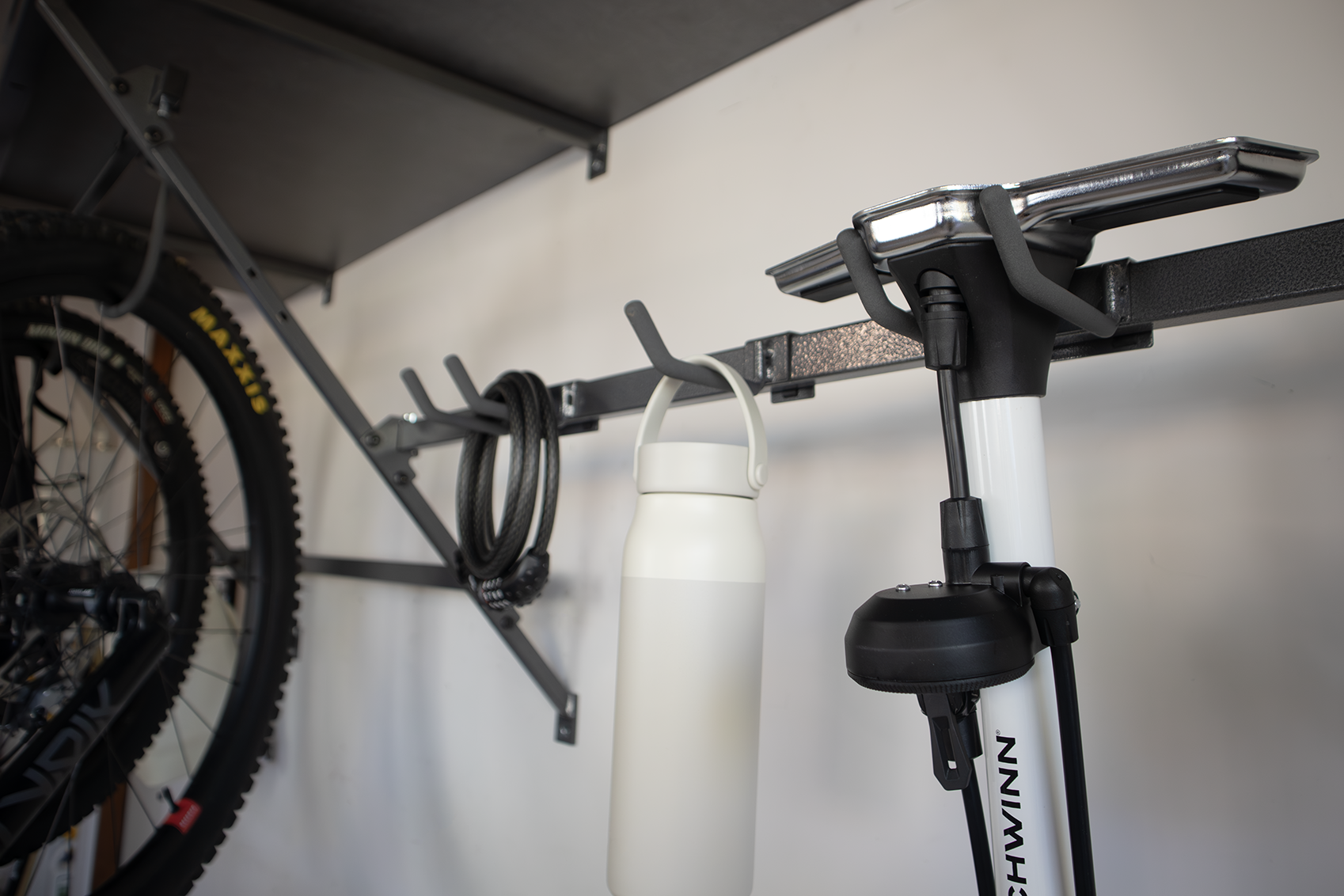 Wall-mounted bike storage with a bicycle wheel, white bottle, and floor pump in a garage or closet