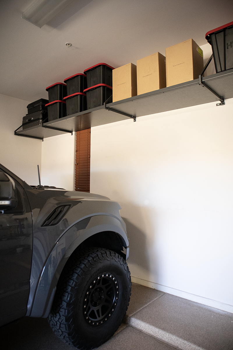 Garage wall shelves with storage bins and boxes above a parked truck