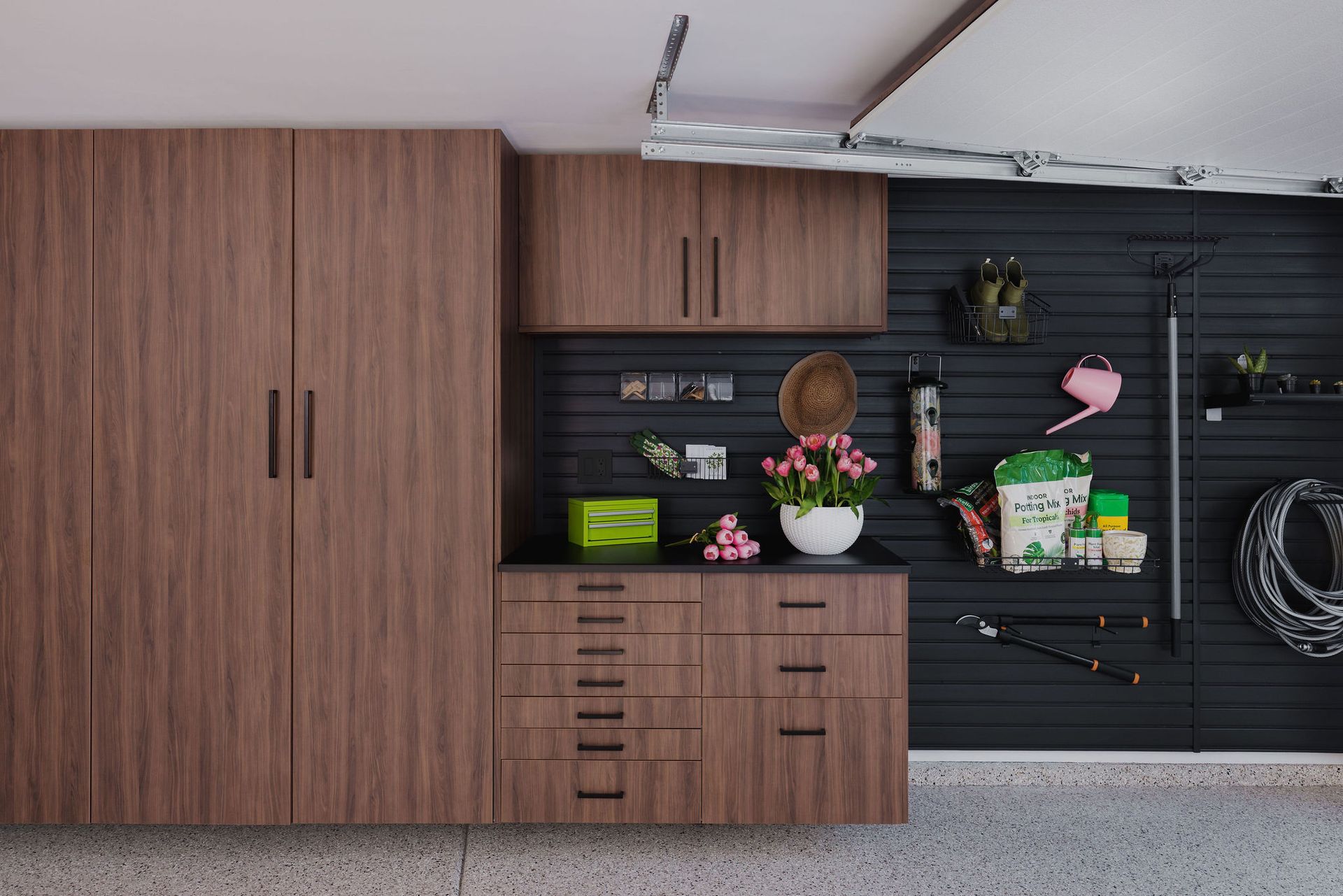 Wood-grain garage cabinets and a black slat wall organized with tools, supplies, and potted flowers.