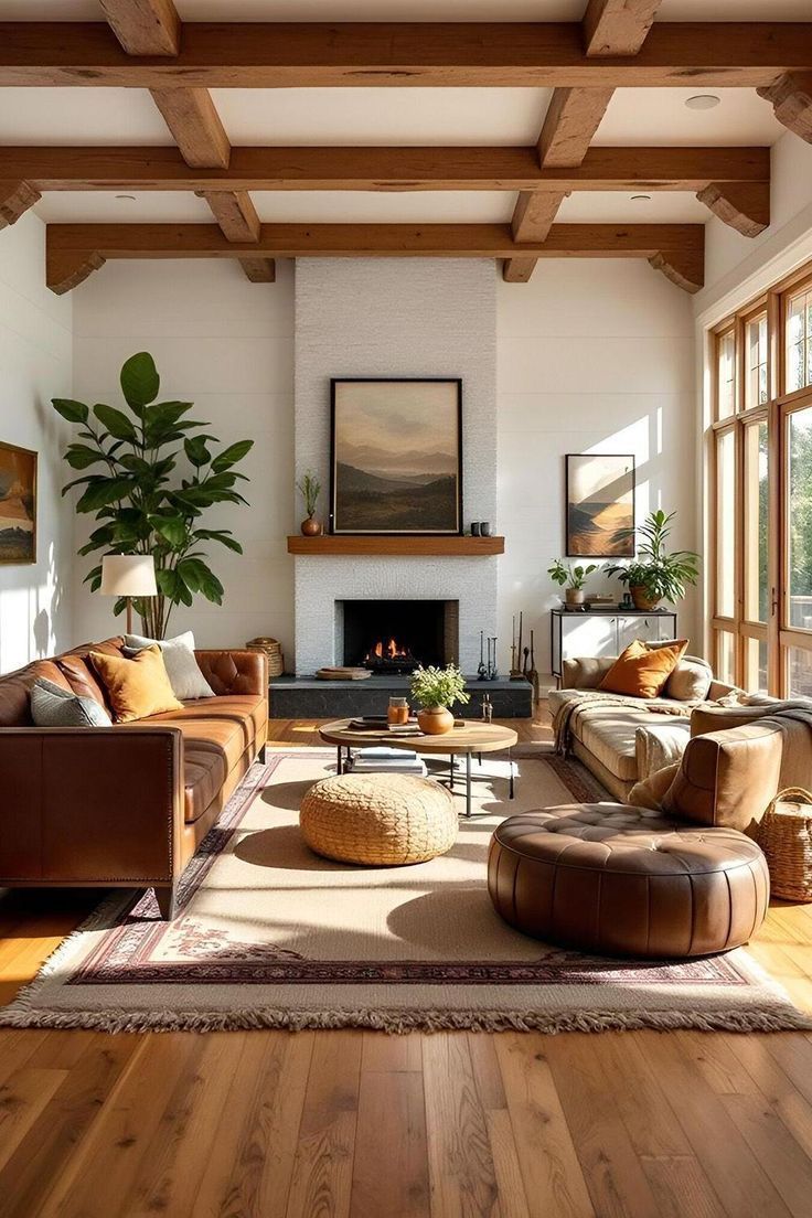 Cozy living room with a fireplace, leather furniture, wooden beams, and large windows. Sunlight streams in, illuminating the space.