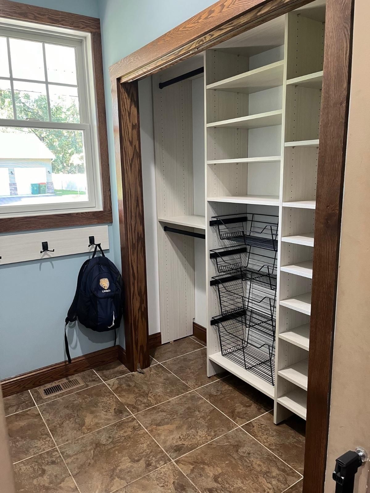 A closet with lots of shelves and a backpack hanging on the wall.