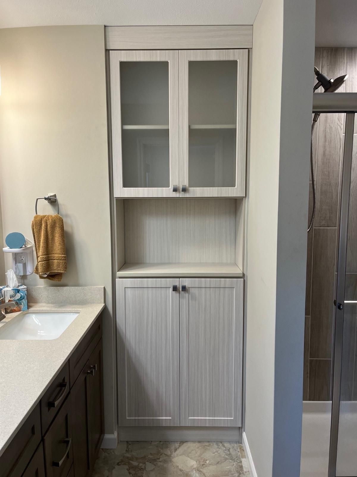 A bathroom with a sink , cabinets , and glass doors.