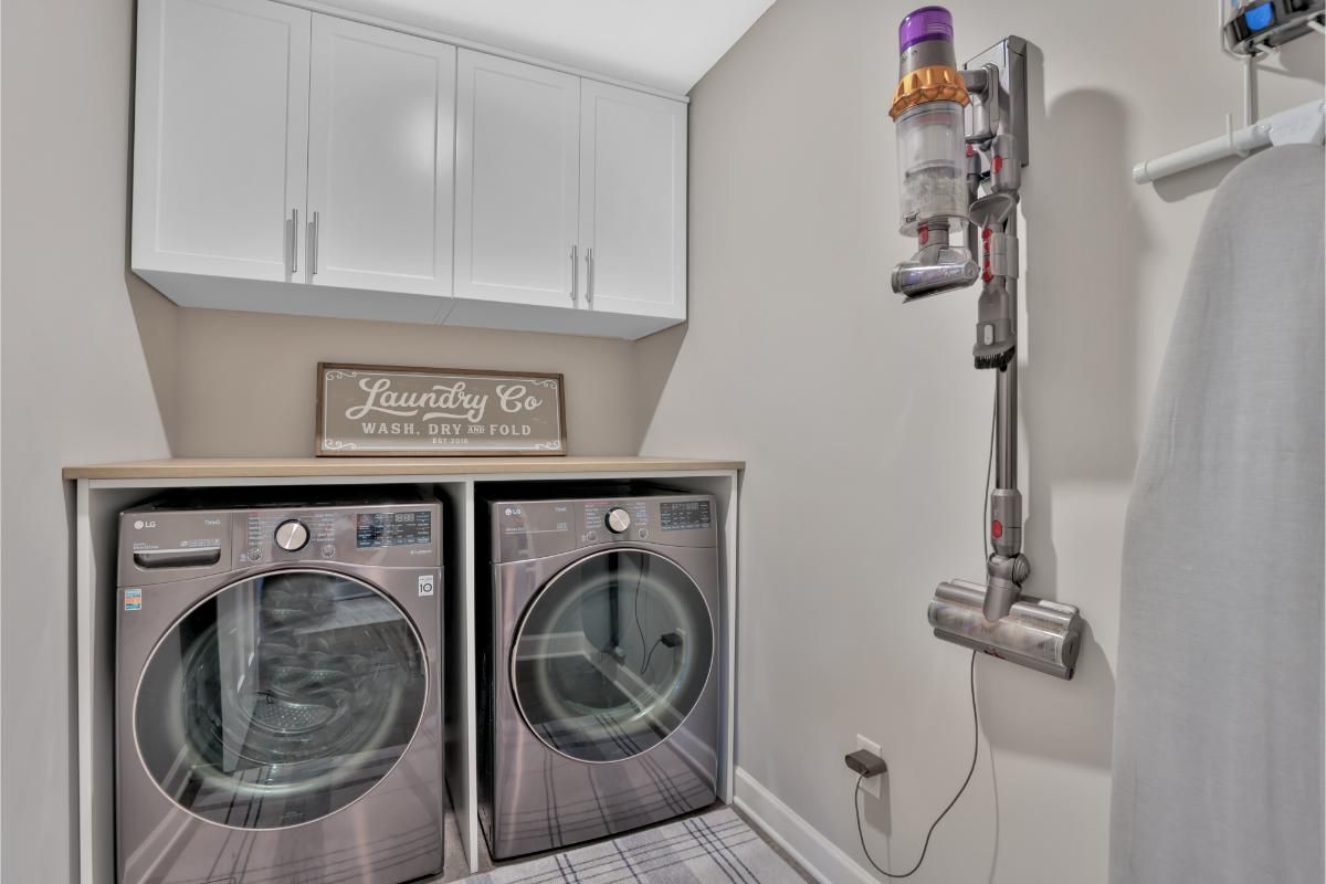 A laundry room with a washer and dryer and a vacuum cleaner hanging from the wall.