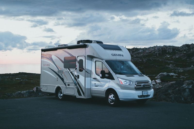 White RV camper parked on a dark road at dusk with cloudy sky and open side door