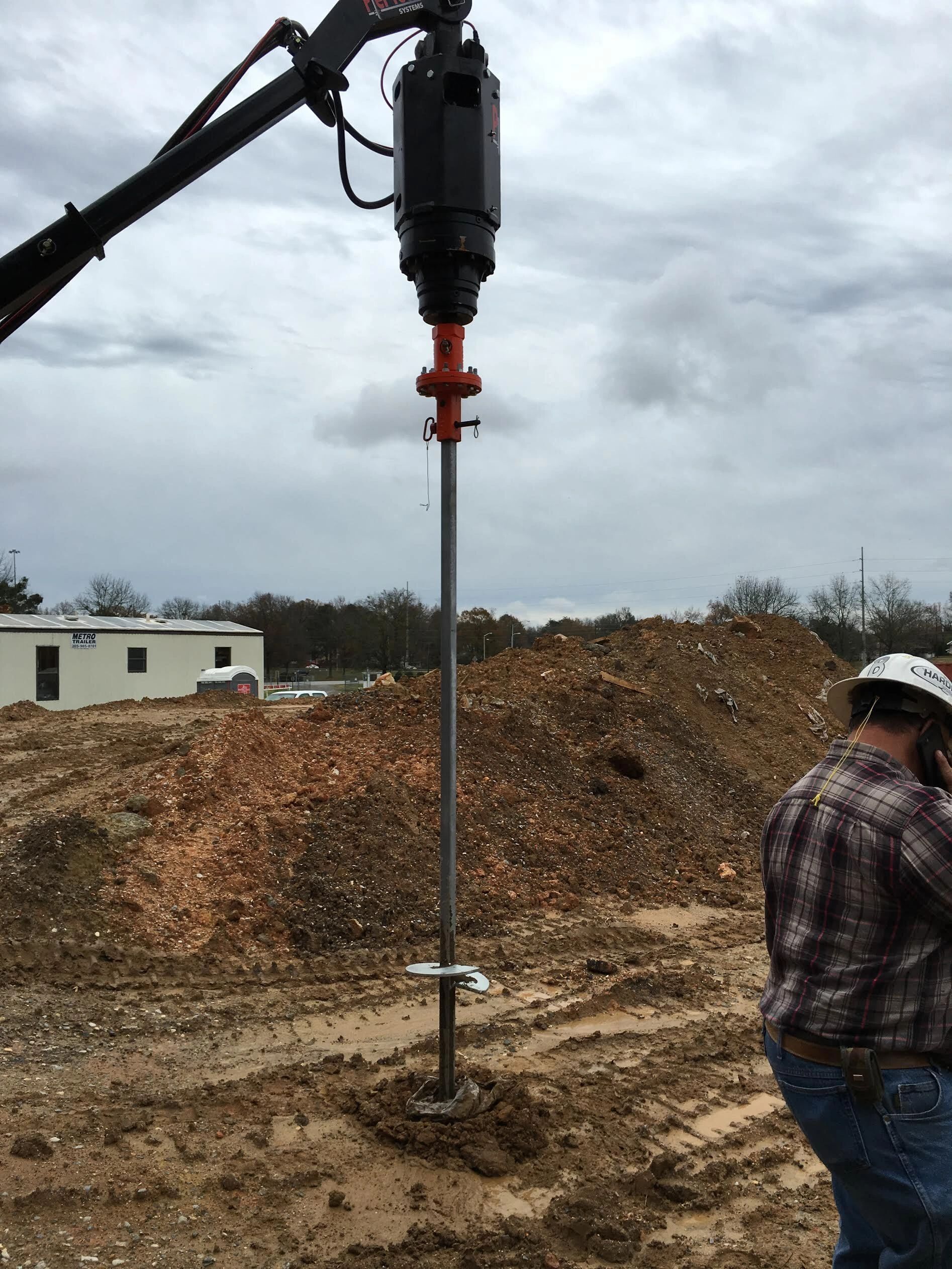 A man wearing a hard hat is standing next to a drill in the dirt