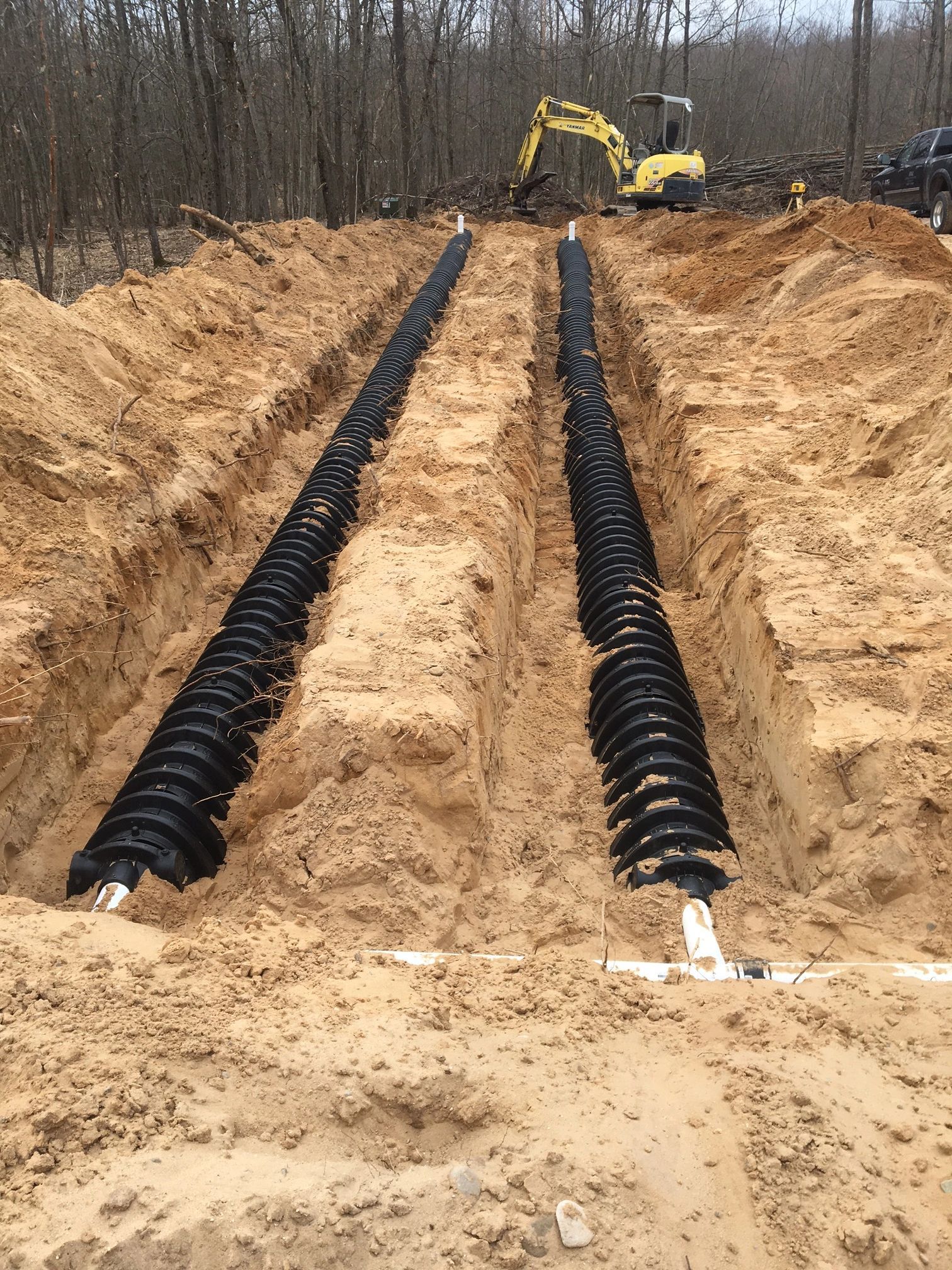A yellow excavator is digging a trench for a septic system.