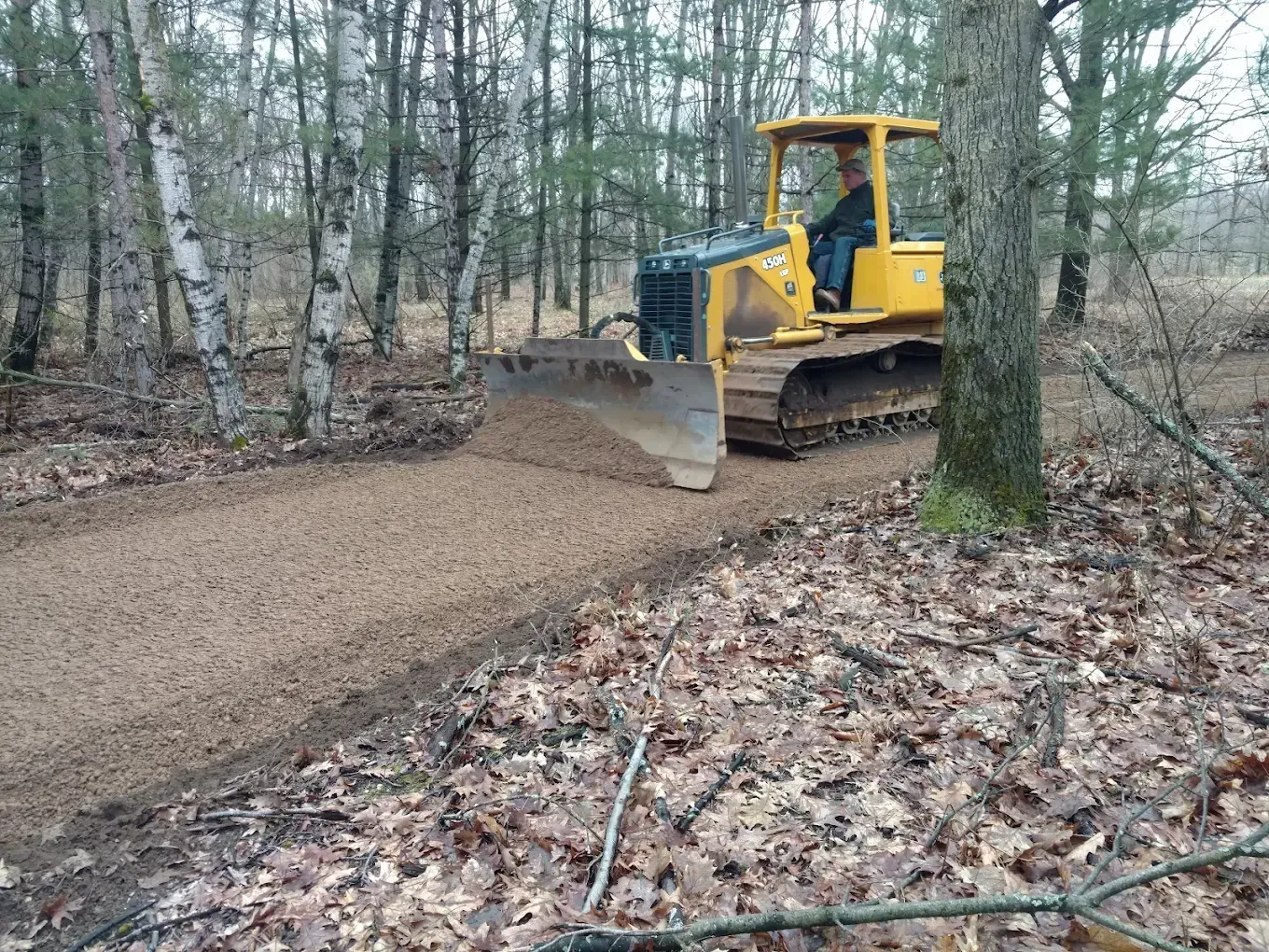 A bulldozer is driving down a dirt road in the woods.