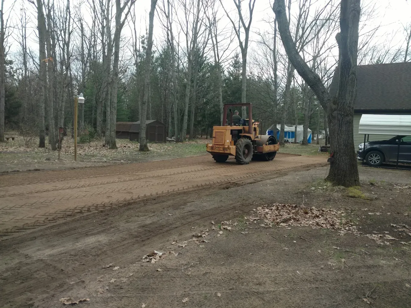 A tractor is driving down a dirt road next to a garage.