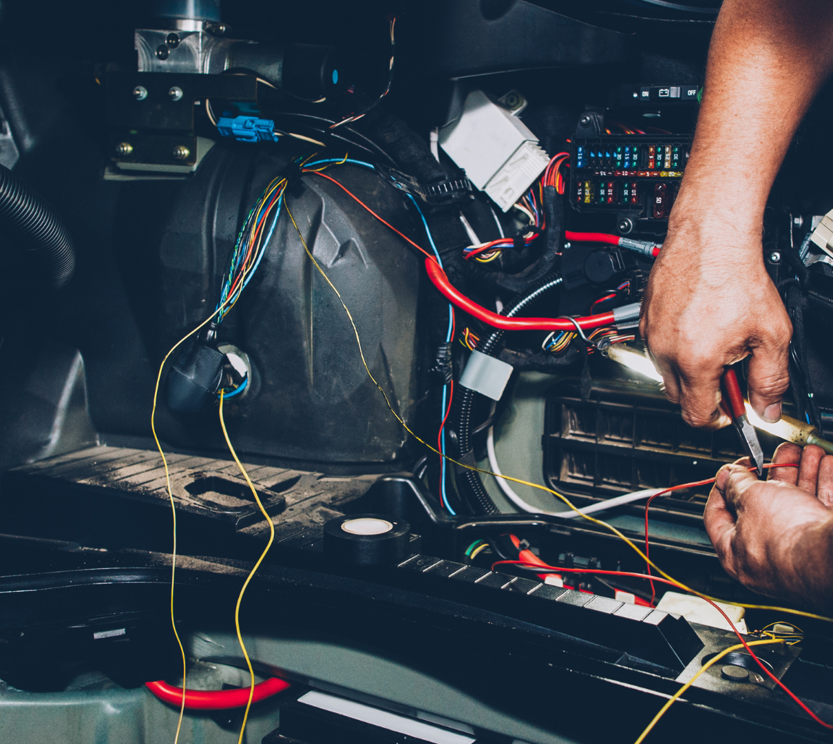 A man is working on a car with a pair of pliers.