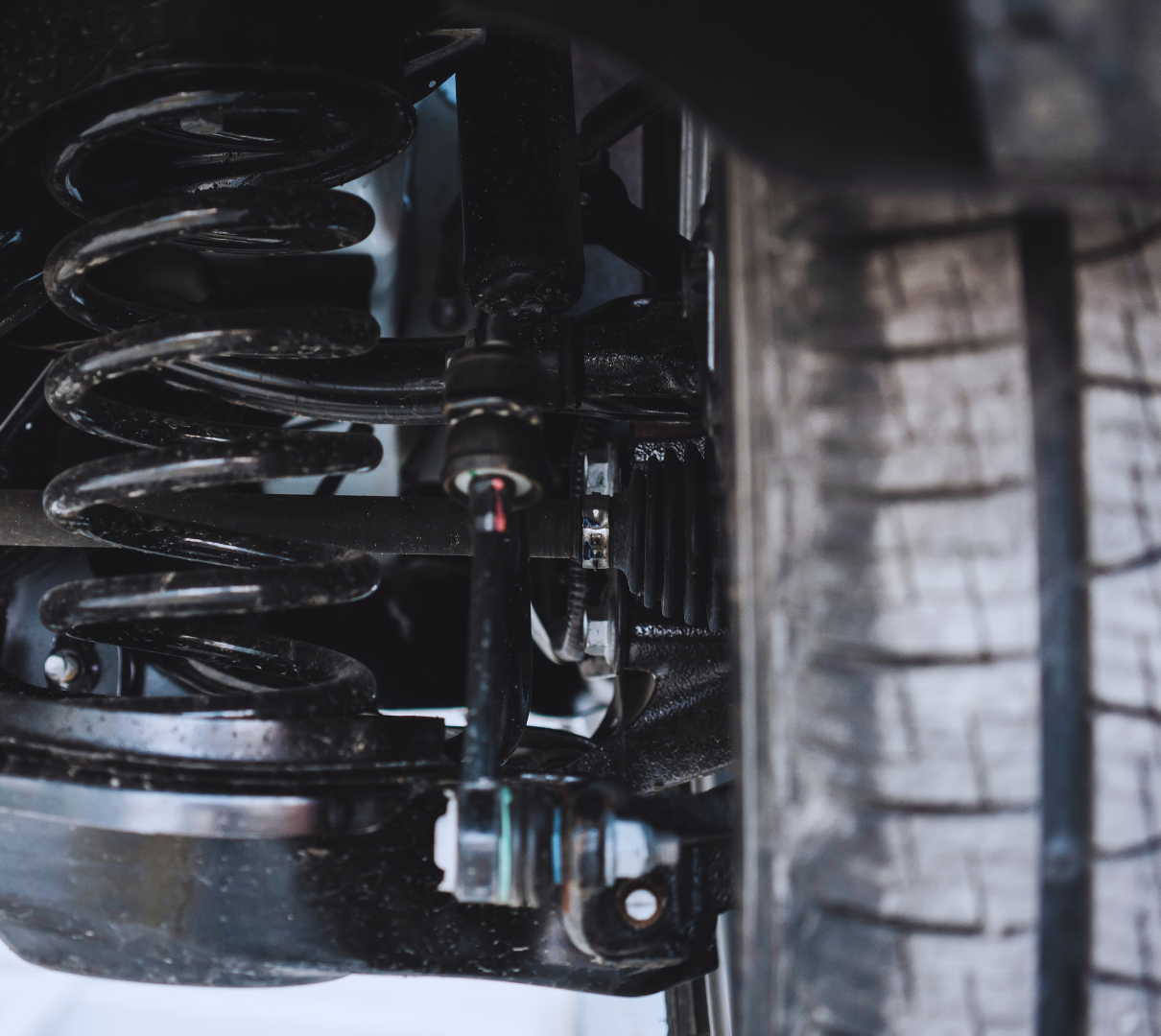 A close up of a car suspension with a tire in the background.