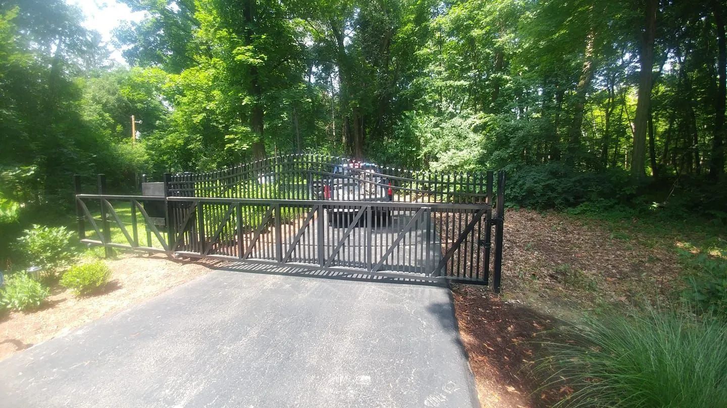 Black metal gate across a paved driveway in a leafy wooded area
