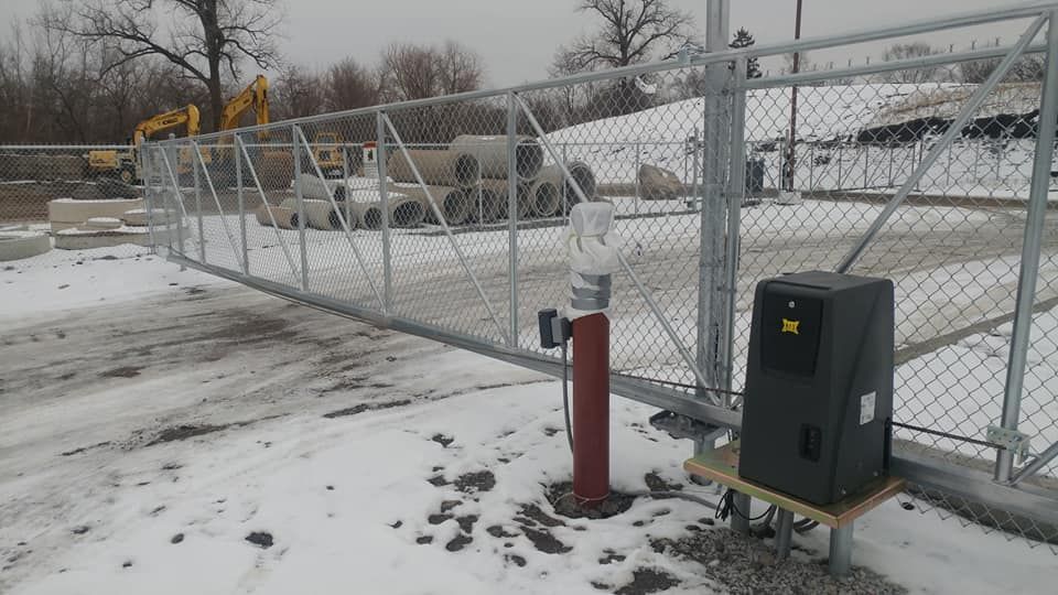 Snowy industrial fence gate with red bollard and gray utility box