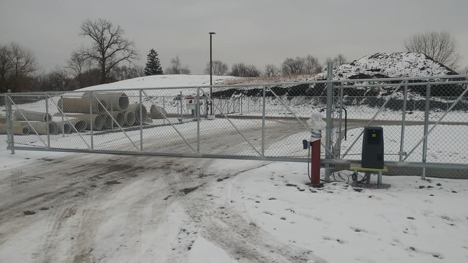 Snow-covered gated entrance on a cloudy day, with a red fire hydrant and trash bin in front
