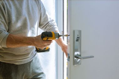 Person using a yellow power drill to install a silver door handle on a white door