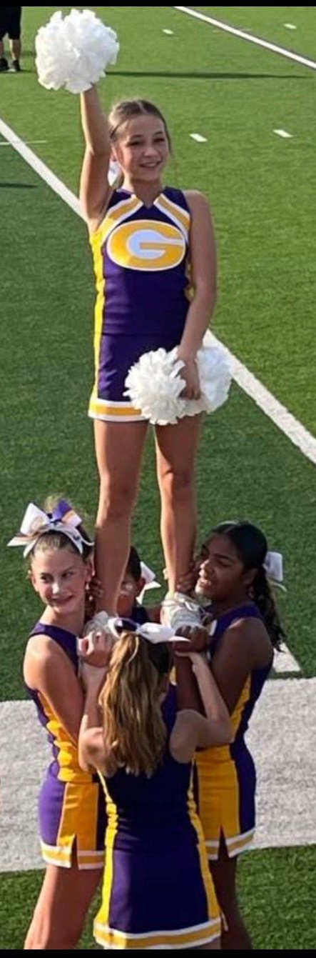 Football players in action on a grassy field; one runs with the ball, pursued by two opponents.