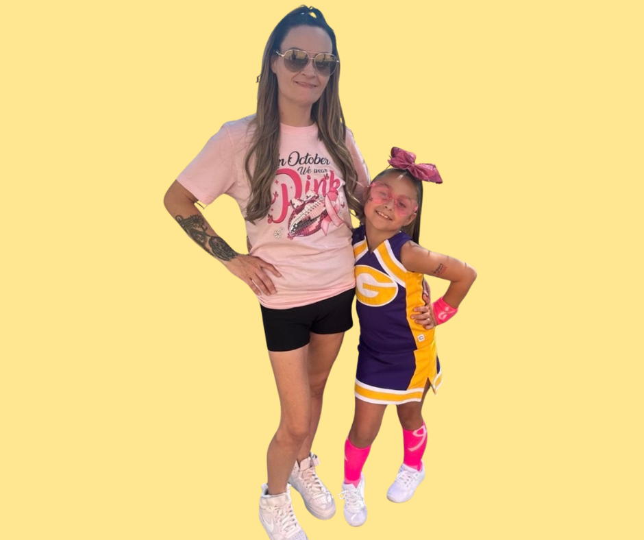 Football coach, arms crossed, on the field. Blue shirt, serious expression, players in background.