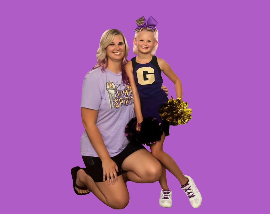 Football coach, arms crossed, on the field. Blue shirt, serious expression, players in background.