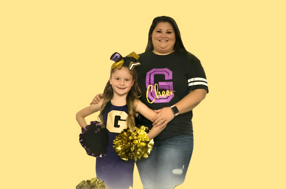 Man in green polo stands on a football field, arms crossed, stadium in background.