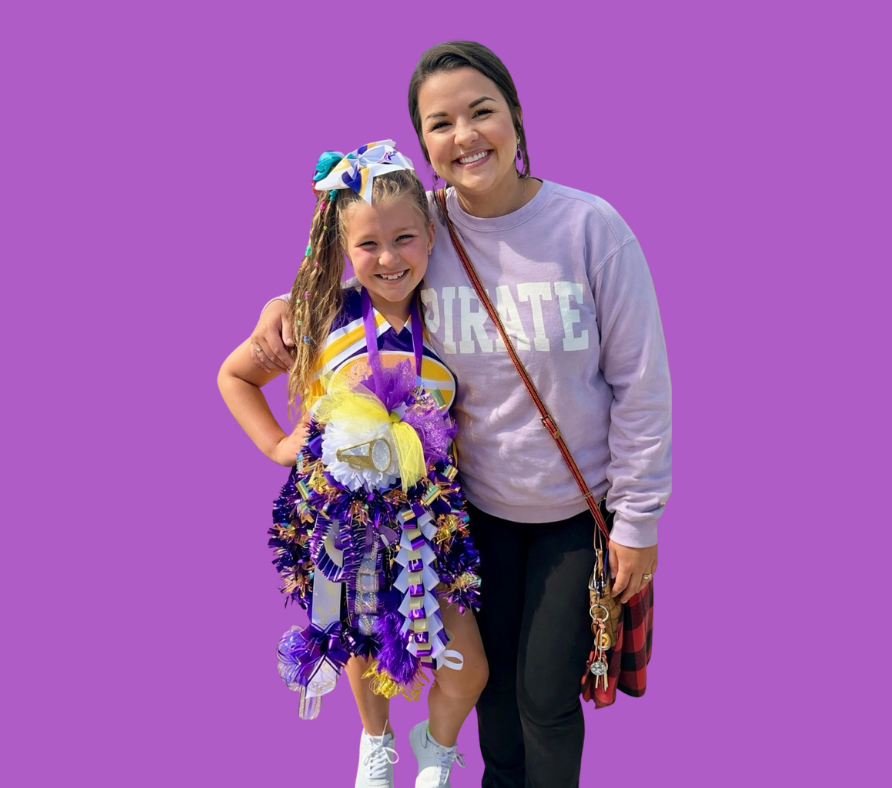 Man with crossed arms on a football field. He is wearing a blue polo shirt, khaki pants, and has a serious expression.