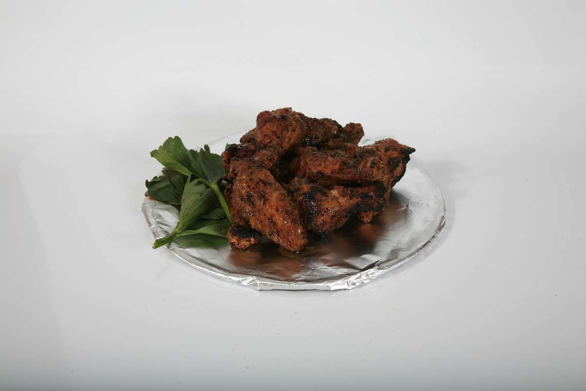A plate of fried chicken wings with parsley on a white background.
