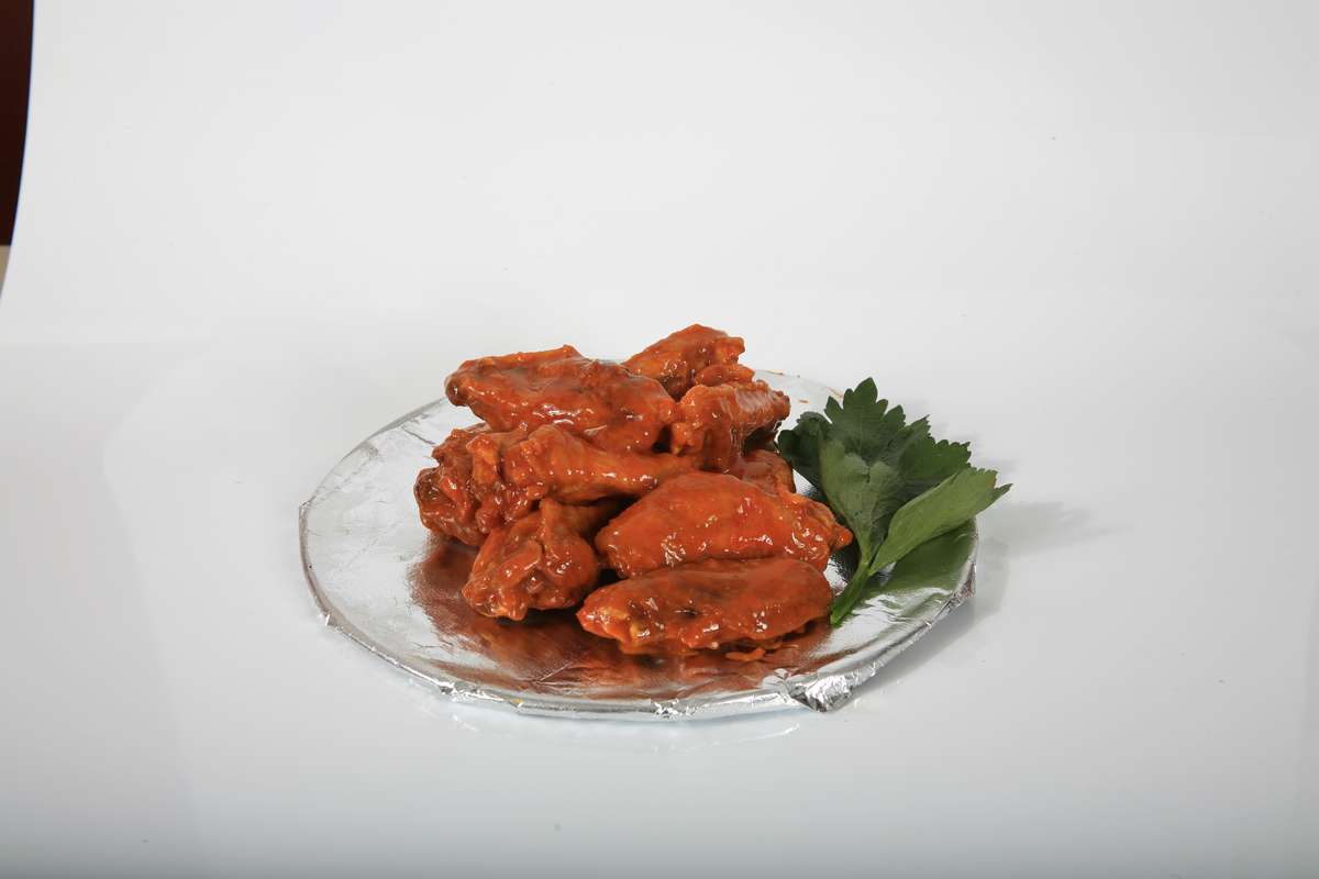 A plate of chicken wings with sauce and parsley on a white background.