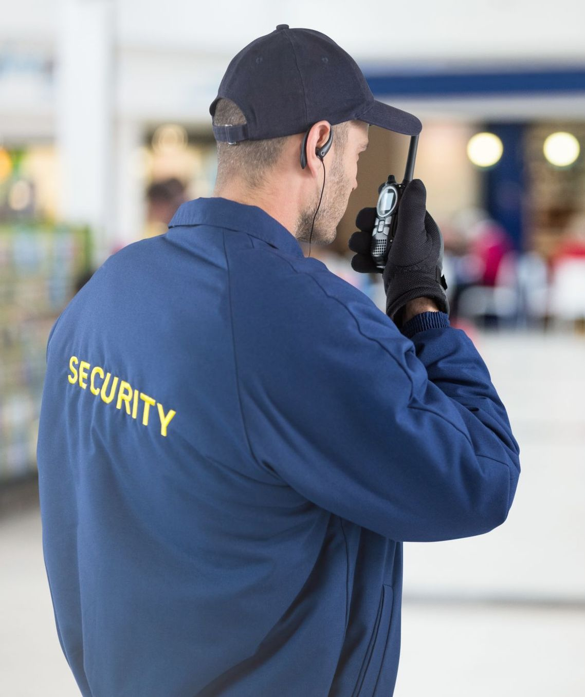 Security guard, in blue uniform, using a walkie-talkie indoors. 