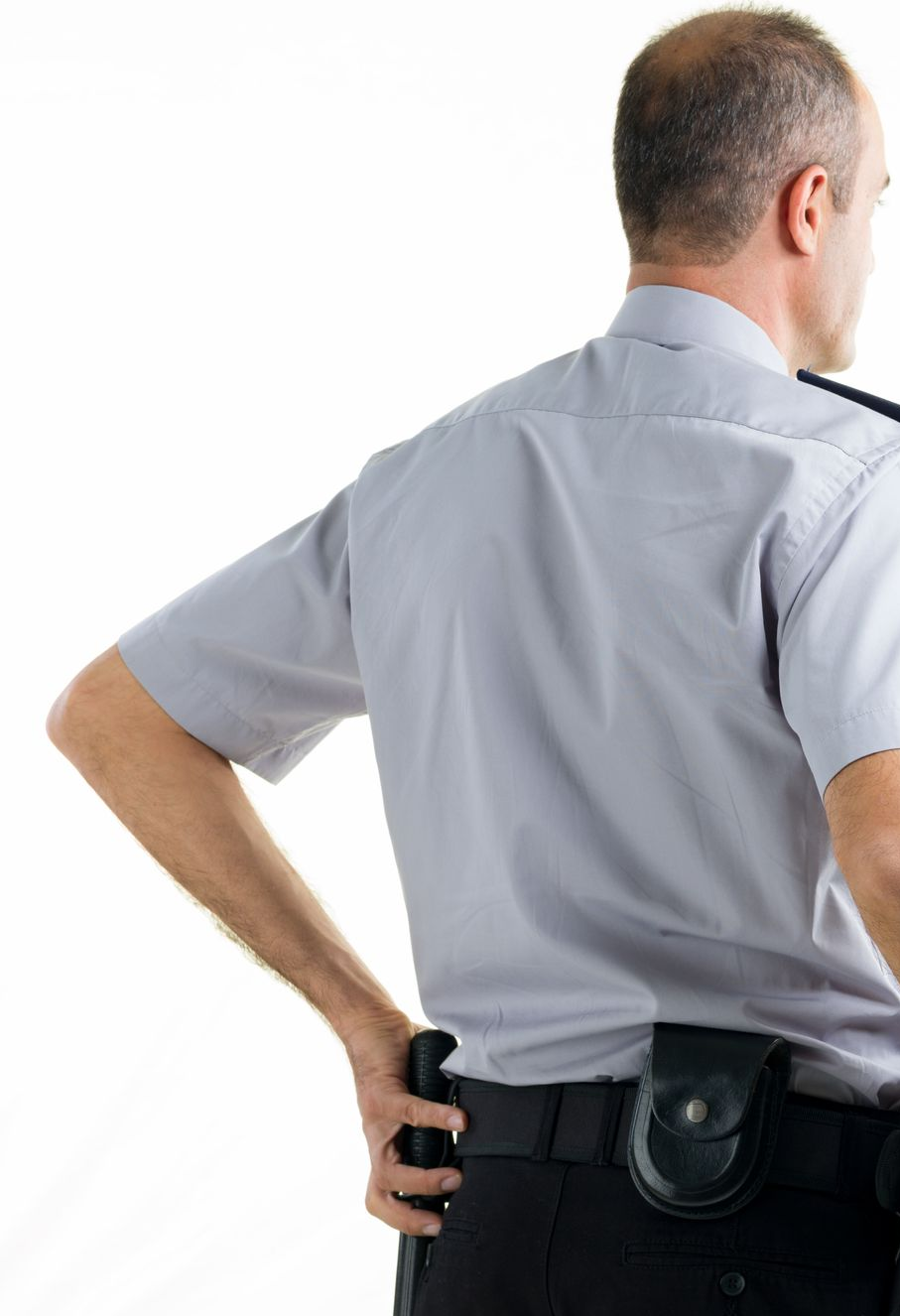 A uniformed person, seen from the back, has hand on holster.