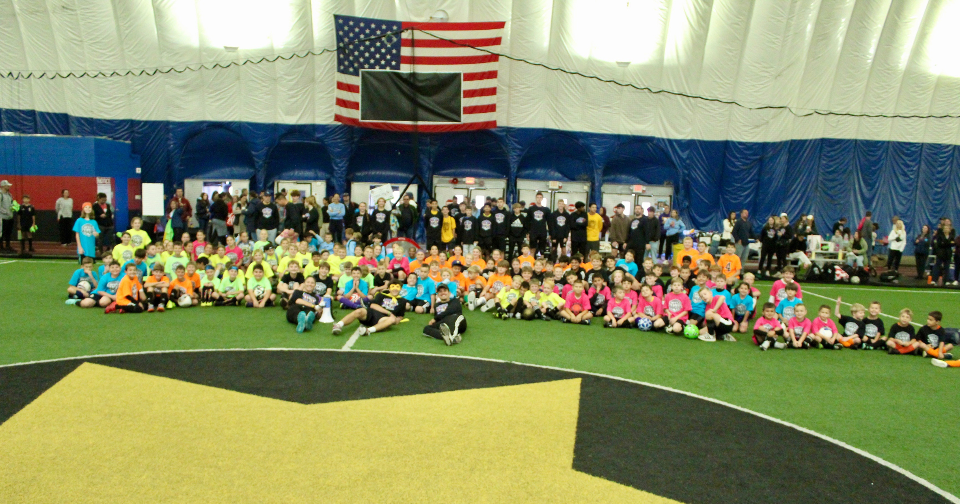 8th Annual JRP 3v3 Soccer Tournament. Large group of kids on a soccer fields under the American Flag