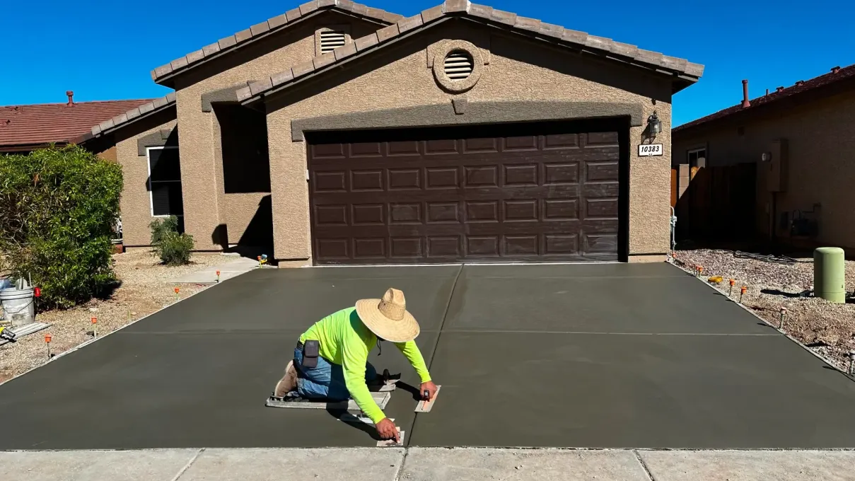 A man is kneeling down in front of a house while working on a driveway.