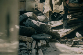 A person is standing next to a pile of tires and wood.