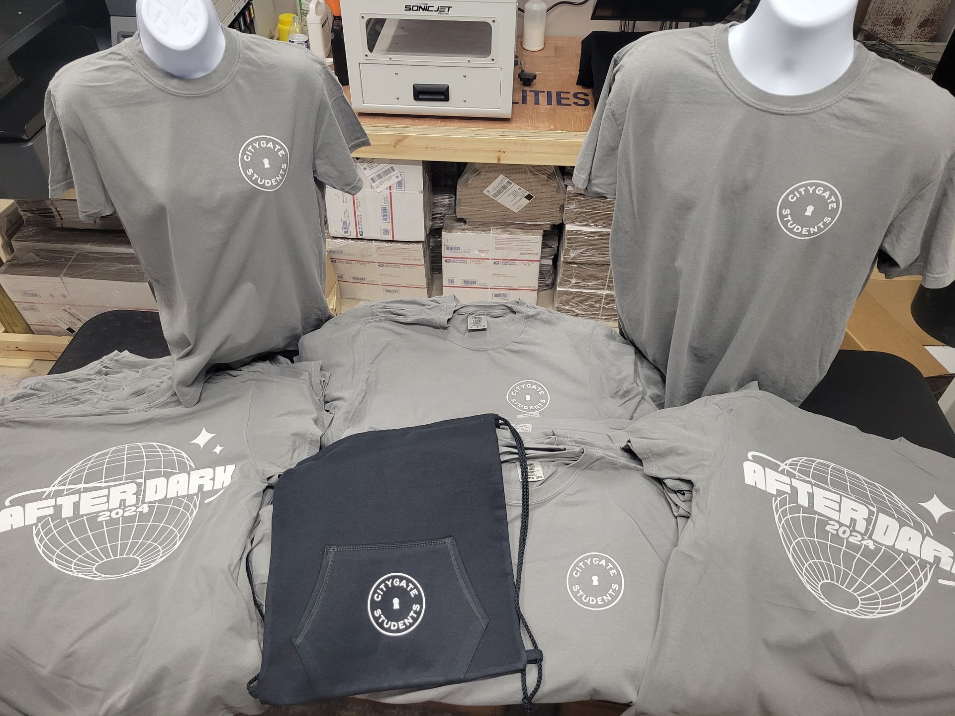 Three t-shirts and a drawstring bag are sitting on a table.