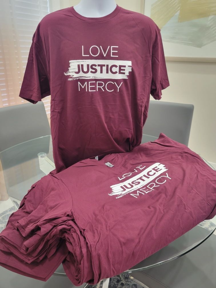 A maroon t-shirt that says `` love justice mercy '' is sitting on a glass table.