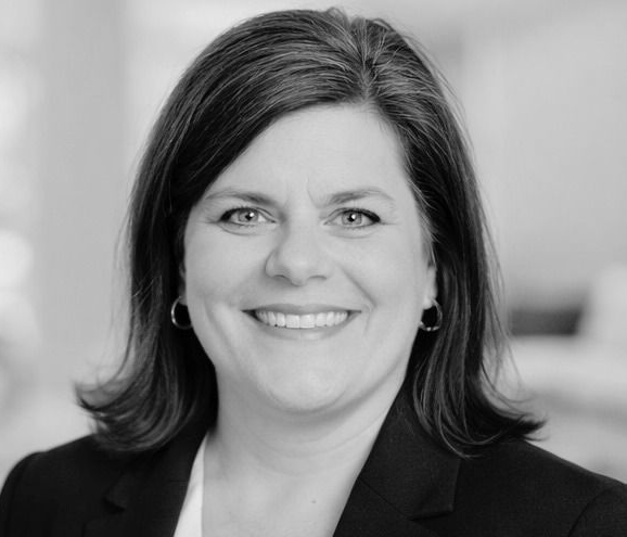 A black and white photo of a woman wearing glasses and smiling.